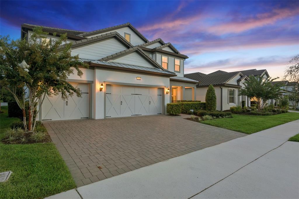A two-story house with a three-car garage and a paved driveway at sunset — 7606 WANDERING WAY, ORLANDO, FL