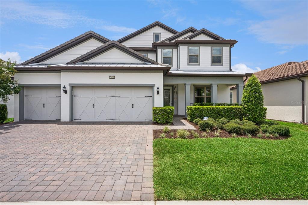 A two-story house with a three-car garage, white stucco walls, and a paved driveway — 7606 WANDERING WAY, ORLANDO, FL