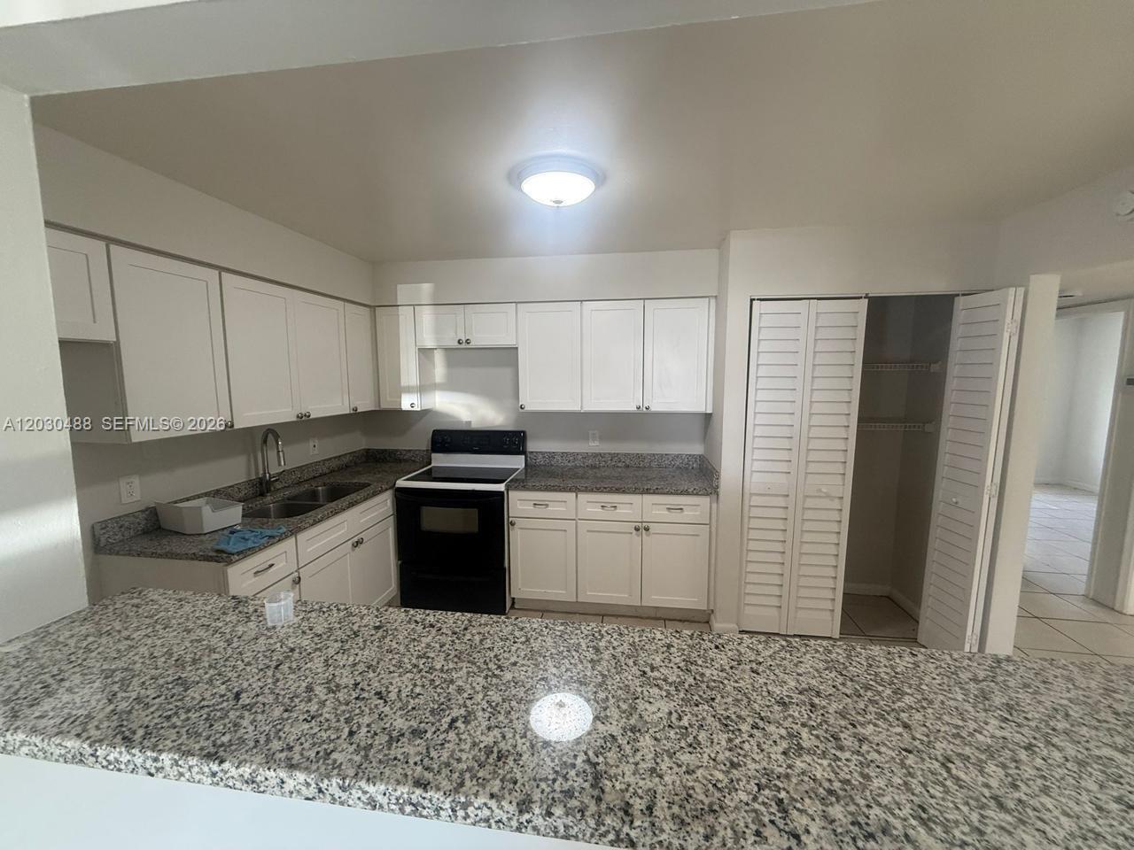 A kitchen features white cabinets, granite countertops, a black stove, and a pantry closet — RIVIERA BEACH, FL