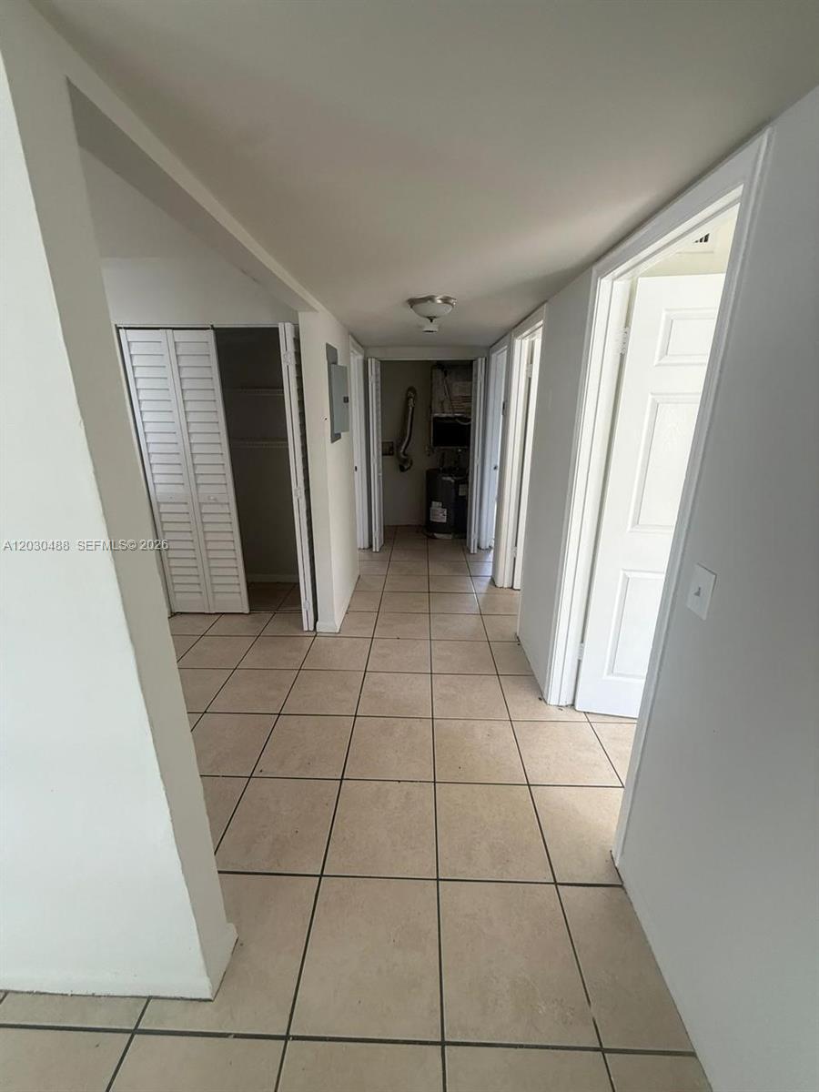 A hallway with beige tile flooring leads to a utility closet at the end — RIVIERA BEACH, FL