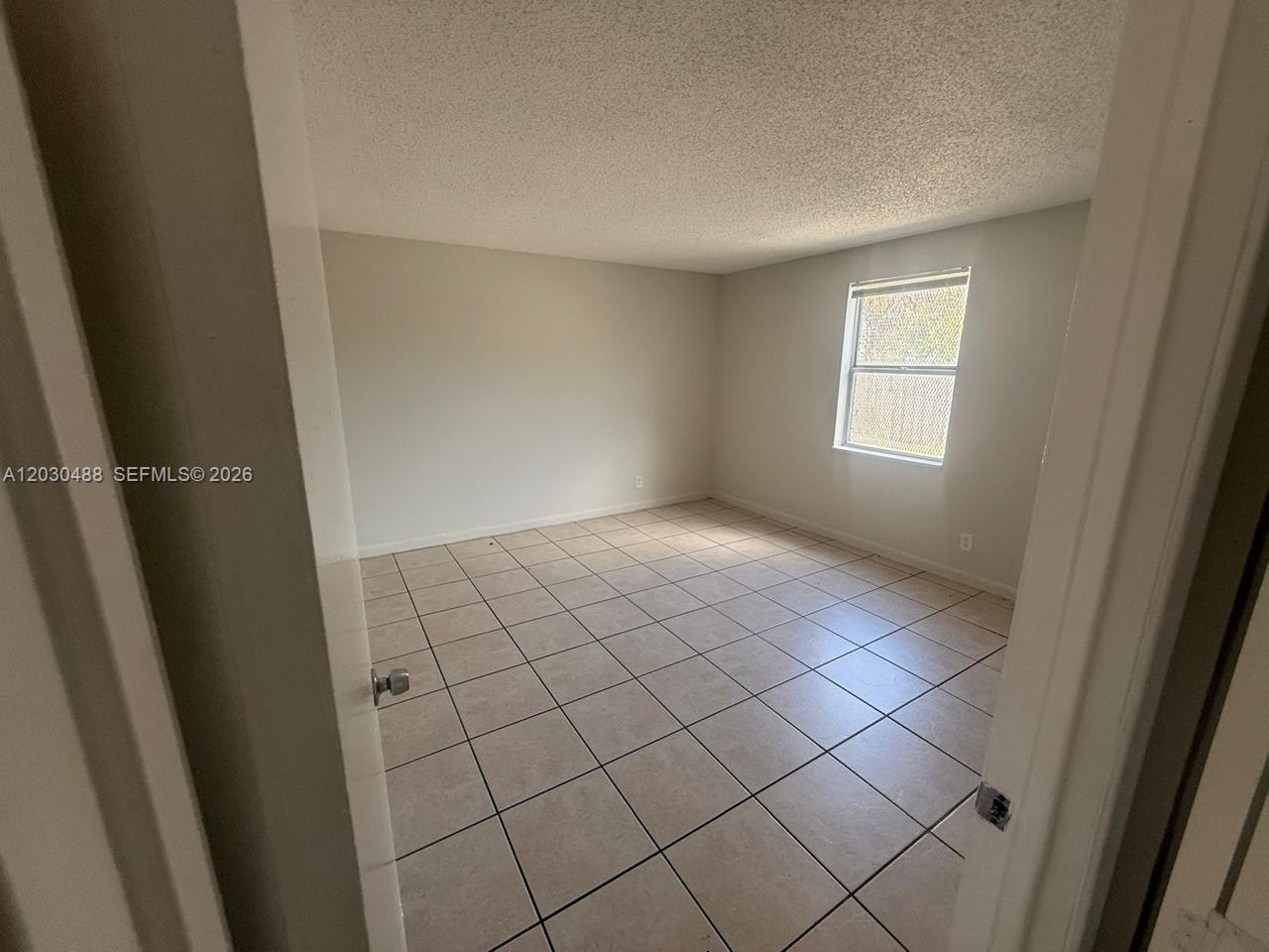 An empty bedroom features light-colored tile flooring, white walls, and a single window — RIVIERA BEACH, FL