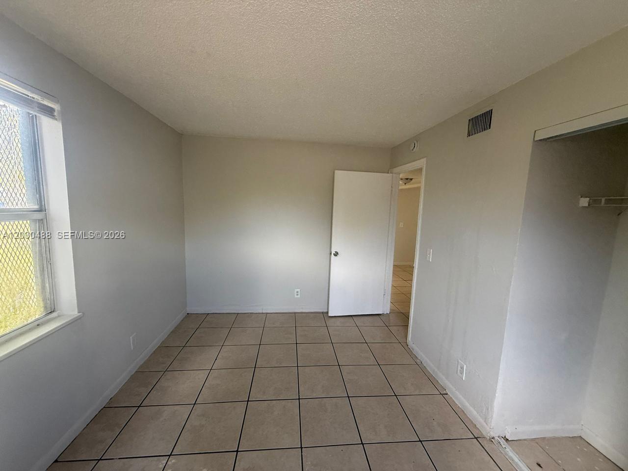 An empty bedroom features light-colored walls, a tiled floor, a window, and a closet — RIVIERA BEACH, FL