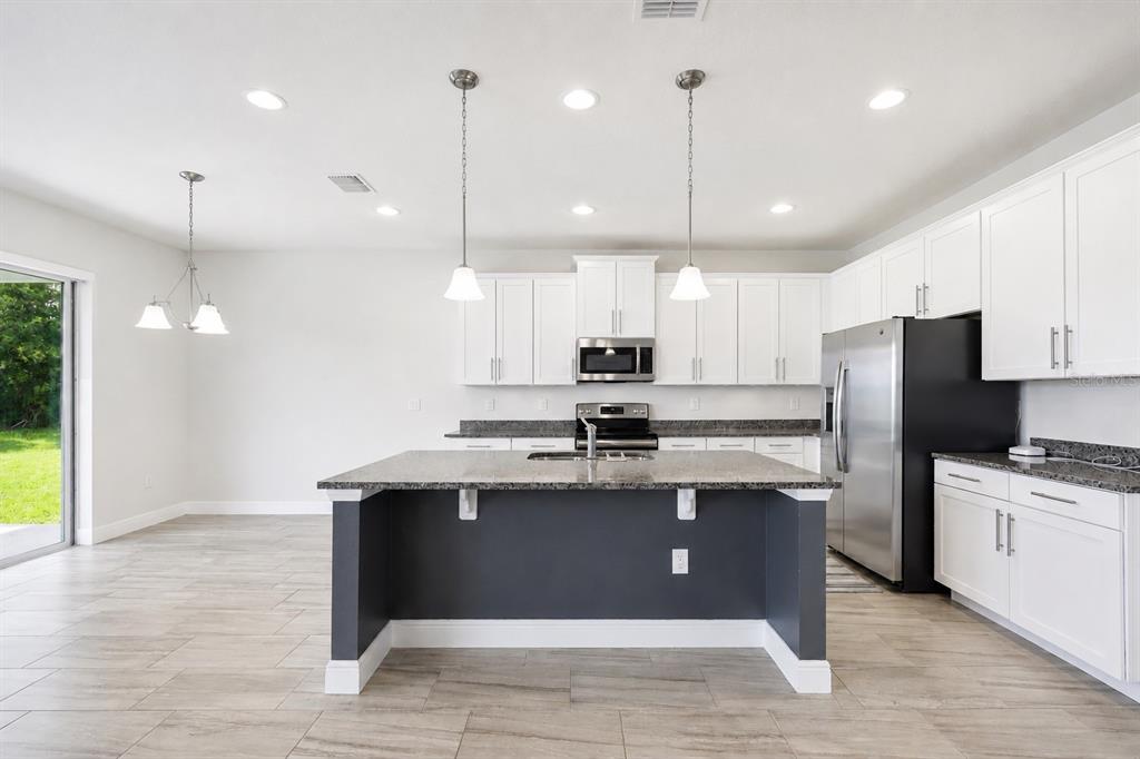 A kitchen features white cabinets, a dark gray island, stainless steel appliances, and tile flooring — 4424 SILVER CREEK STREET, KISSIMMEE, FL