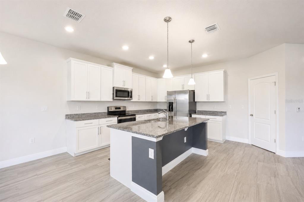 A kitchen features white cabinetry, granite countertops, a dark gray island, and light wood-look flooring — 4424 SILVER CREEK STREET, KISSIMMEE, FL