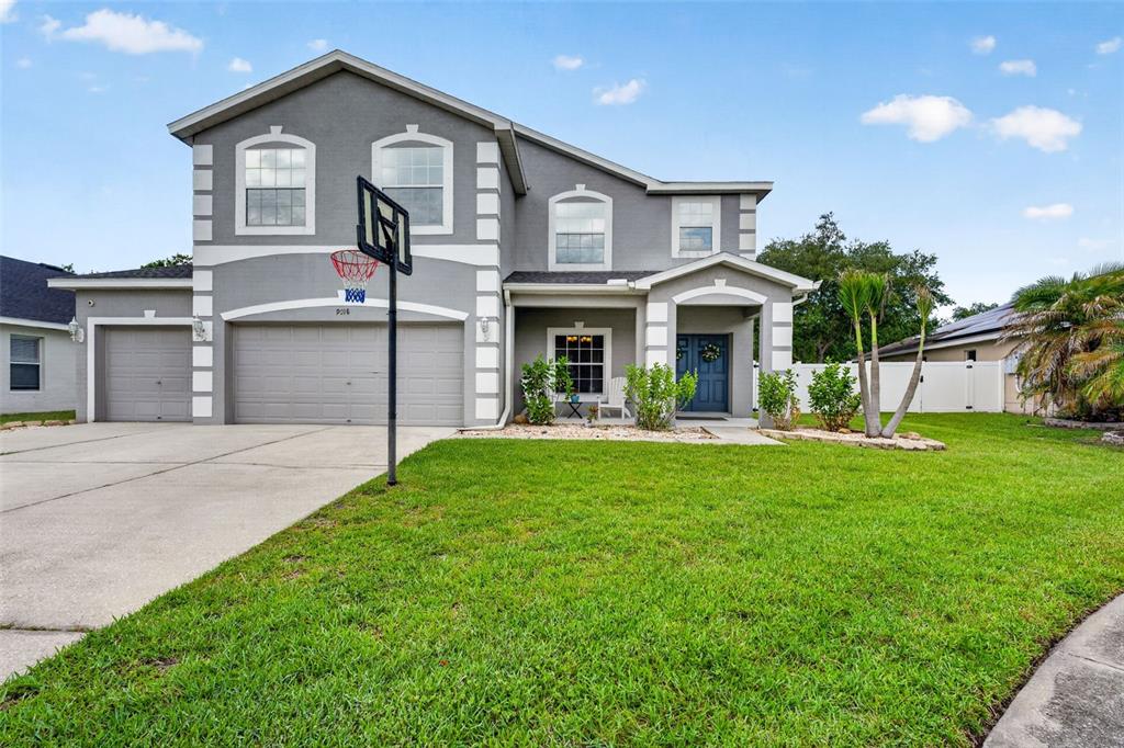 A two-story gray house with a three-car garage and a basketball hoop in the driveway — 9018 N RIVER ROAD, TAMPA, FL