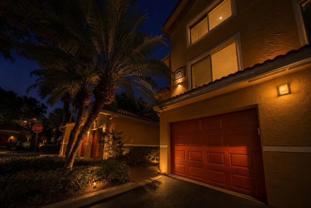 A two-story building exterior at night featuring a red garage door and palm trees — 500 Scotia Drive # 302, Hypoluxo FL 33462, HYPOLUXO, FL