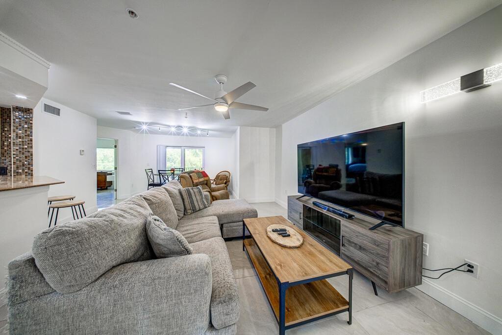 A living room features a grey sectional sofa, a wooden coffee table, and a large television — 500 Scotia Drive # 302, Hypoluxo FL 33462, HYPOLUXO, FL