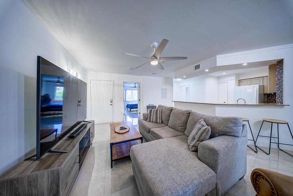 A living room features a grey sectional sofa, a television, and an open kitchen area — 500 Scotia Drive # 302, Hypoluxo FL 33462, HYPOLUXO, FL