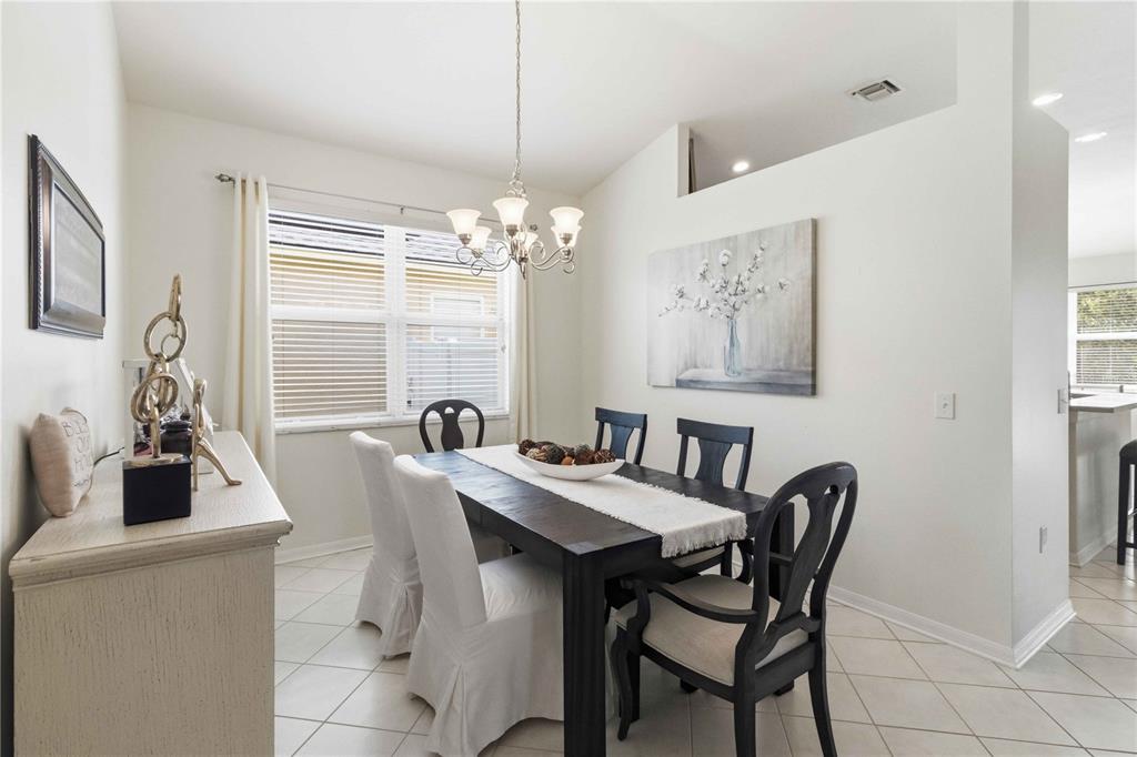 A dining room features a dark wood table, white slipcovered chairs, and a chandelier — 35124 DEERFIELD OAKS DRIVE, ZEPHYRHILLS, FL