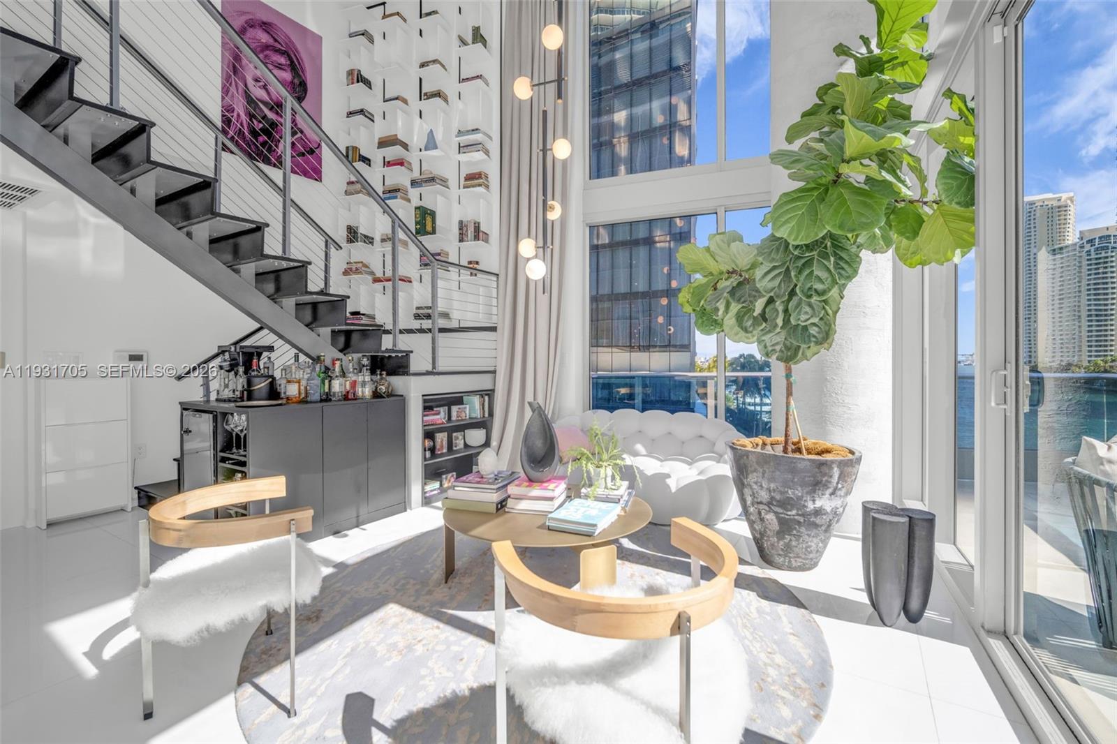 A modern, double-height living room features a floating staircase, floor-to-ceiling windows, and a large plant — 200 Biscayne Boulevard Way # 309, Miami FL 33131, MIAMI, FL
