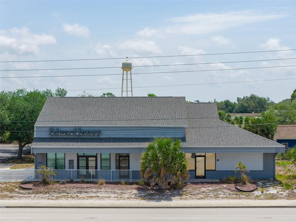 A single-story commercial building with gray siding and a shingled roof stands under a blue sky — 501 S INDIANA AVENUE, ENGLEWOOD, FL