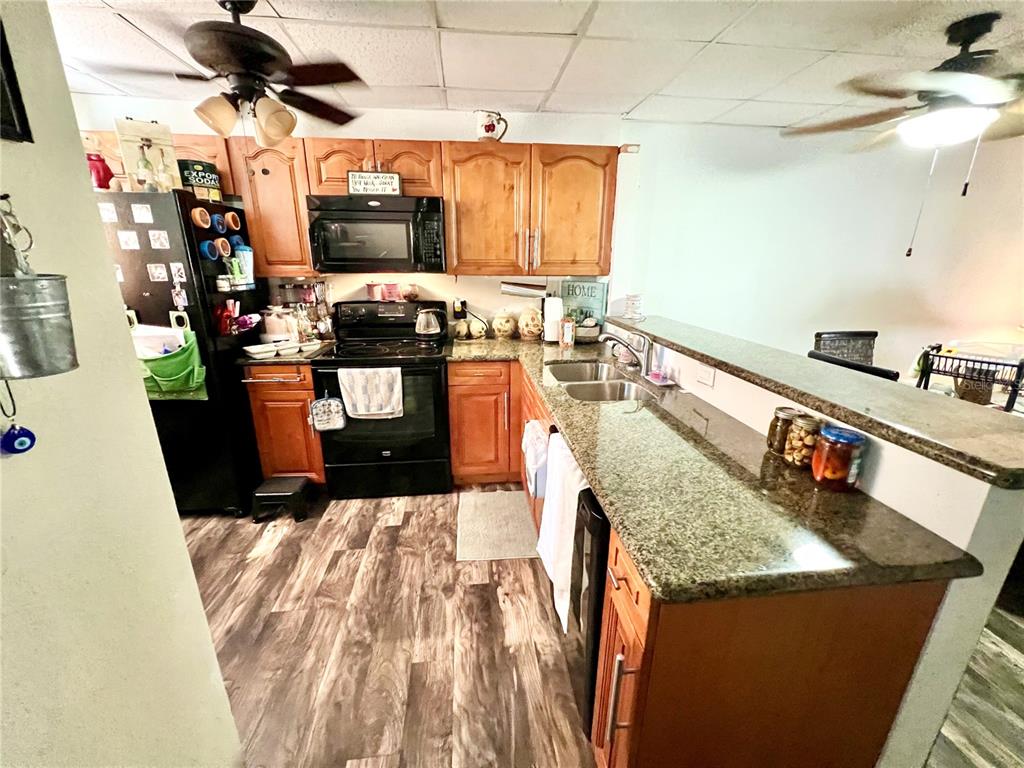 A kitchen features wood cabinets, granite countertops, black appliances, and wood-look flooring — 3116 HARBOR BOULEVARD UNIT 1B, PORT CHARLOTTE, FL