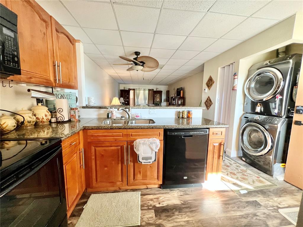 A kitchen features wooden cabinets, granite countertops, a black dishwasher, and a stacked laundry unit — 3116 HARBOR BOULEVARD UNIT 1B, PORT CHARLOTTE, FL