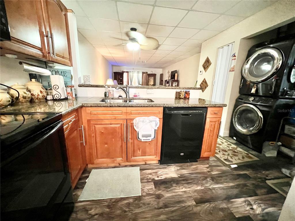 A kitchen features wood cabinets, granite countertops, a black dishwasher, and a stacked laundry unit — 3116 HARBOR BOULEVARD UNIT 1B, PORT CHARLOTTE, FL
