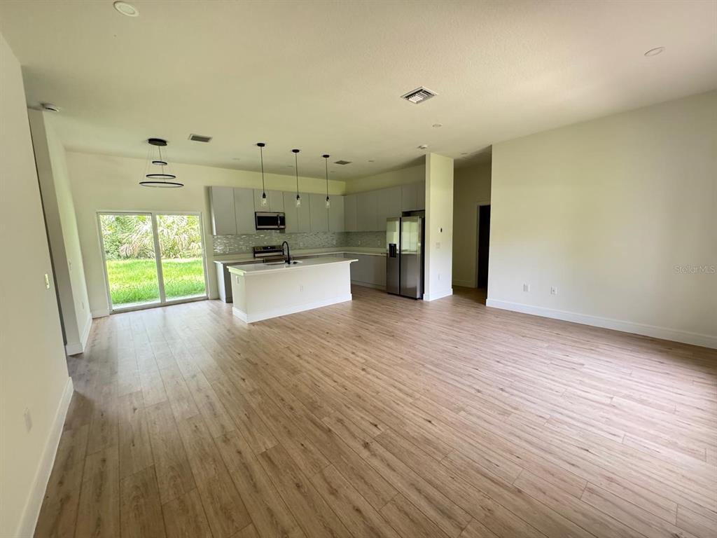 An open-concept kitchen and living area features light wood flooring, gray cabinetry, and sliding doors — 353 WARRINGTON BOULEVARD, PORT CHARLOTTE, FL