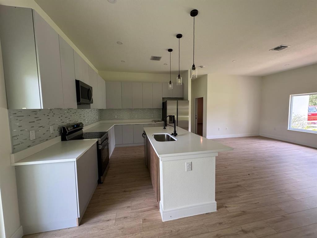 A modern kitchen features light gray cabinets, white countertops, stainless steel appliances, and a central island — 353 WARRINGTON BOULEVARD, PORT CHARLOTTE, FL