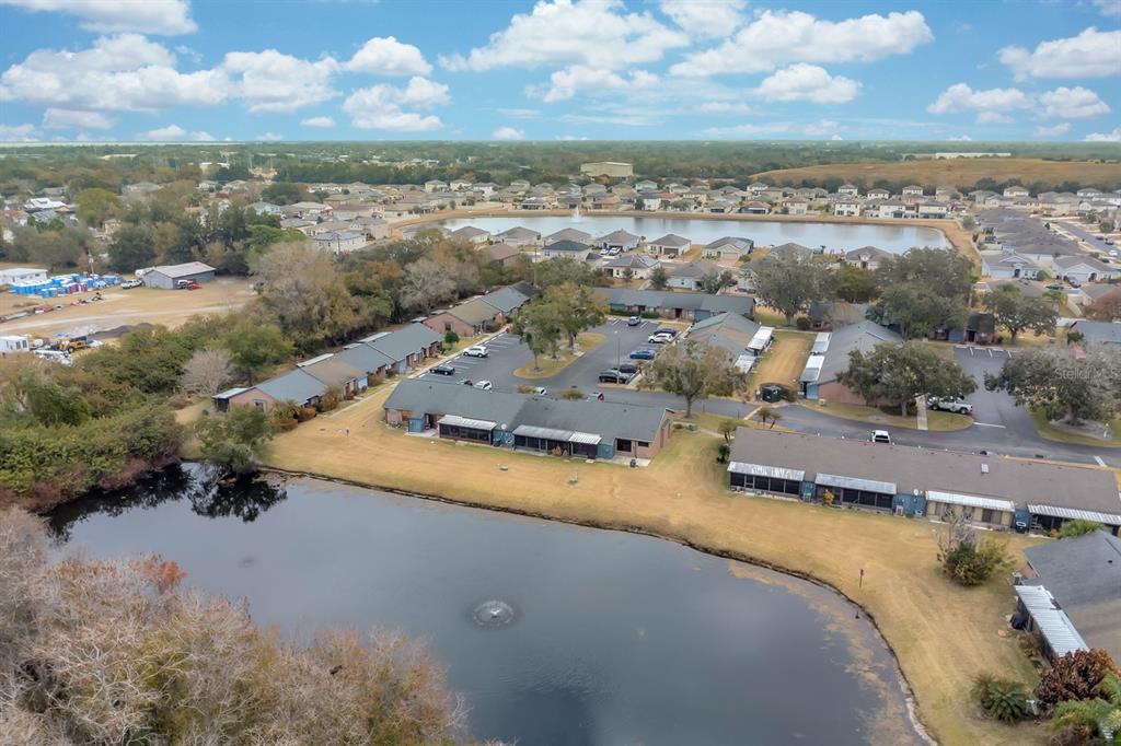 An aerial view shows a residential complex with multiple buildings surrounding a small pond — 2432 KING OAK COURT, ST CLOUD, FL