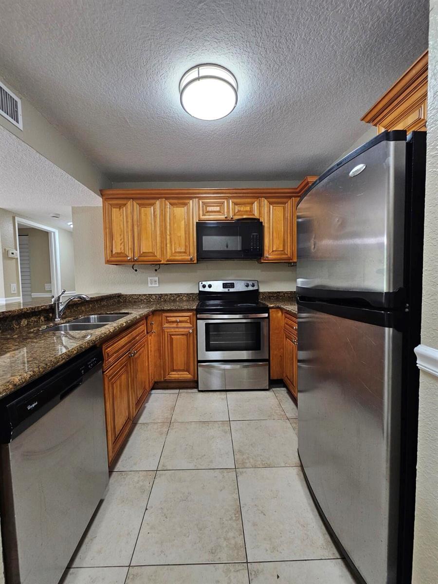 A kitchen features wood cabinets, granite countertops, stainless steel appliances, and light-colored tile flooring — 1541 Windorah Way # C, West Palm Beach FL 33411, WEST PALM BEACH, FL