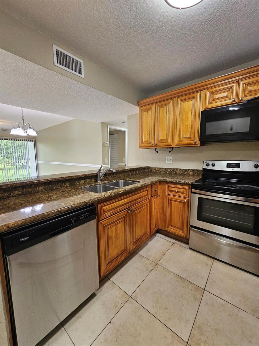 A kitchen with wood cabinets, granite countertops, stainless steel appliances, and tile flooring — 1541 Windorah Way # C, West Palm Beach FL 33411, WEST PALM BEACH, FL