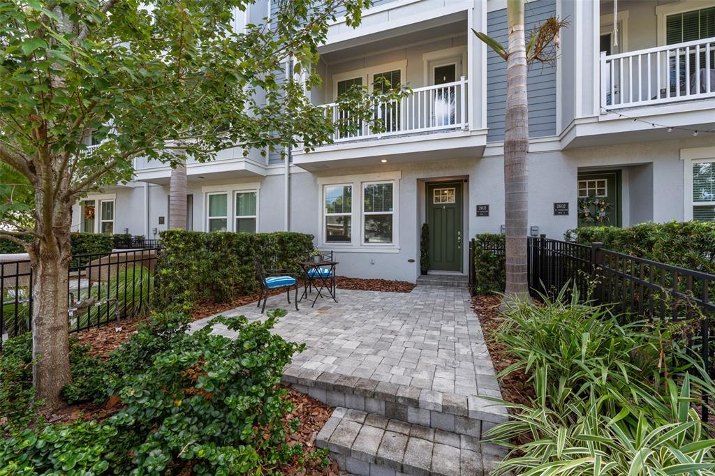 A paved patio leads to the green front door of a multi-story townhouse exterior — 2602 W CLEVELAND STREET UNIT 3, TAMPA, FL