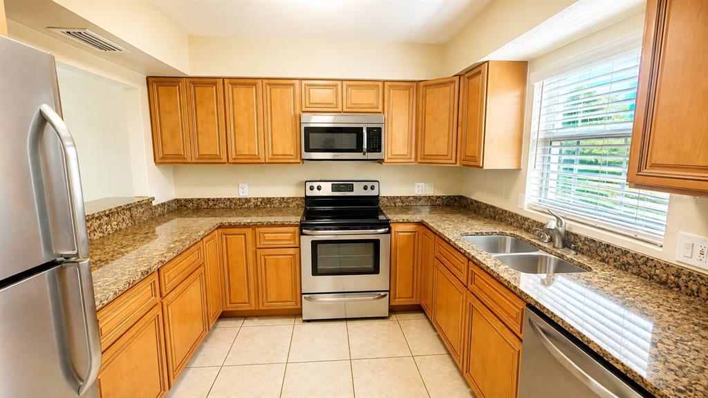 A kitchen features wood cabinets, granite countertops, stainless steel appliances, and light-colored tile flooring — 2405 ASPINWALL STREET UNIT 2405, SARASOTA, FL