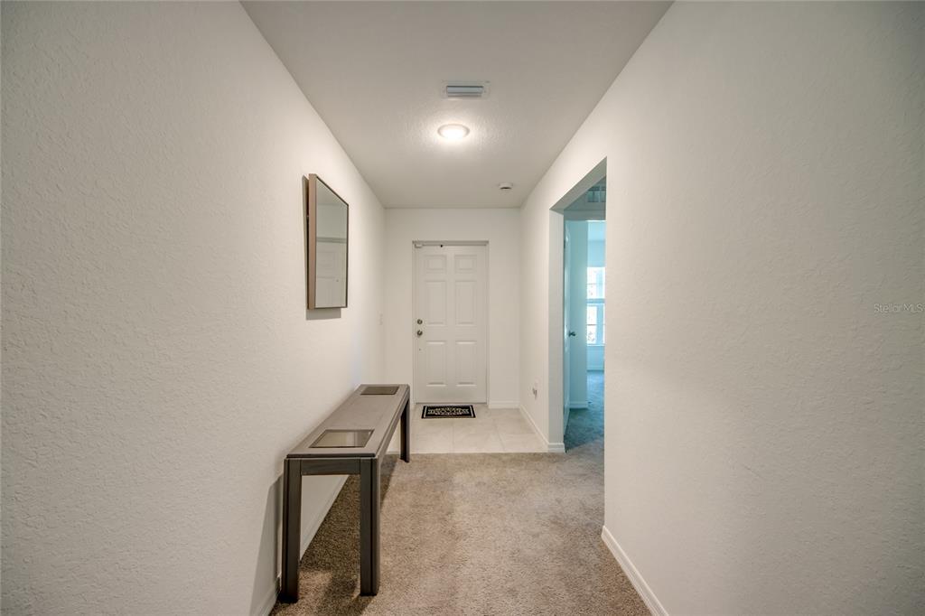 A carpeted entryway features a console table, a wall mirror, and a white front door — 16069 EDINA AVENUE, PORT CHARLOTTE, FL