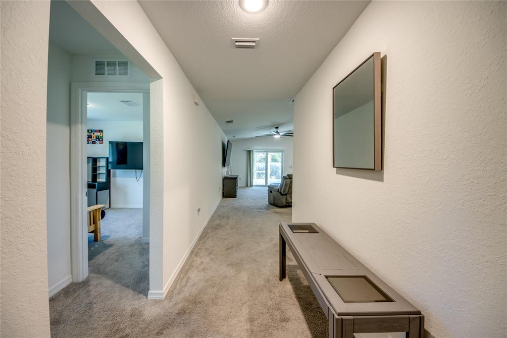 A carpeted hallway leads to an open living area with a sliding glass door — 16069 EDINA AVENUE, PORT CHARLOTTE, FL