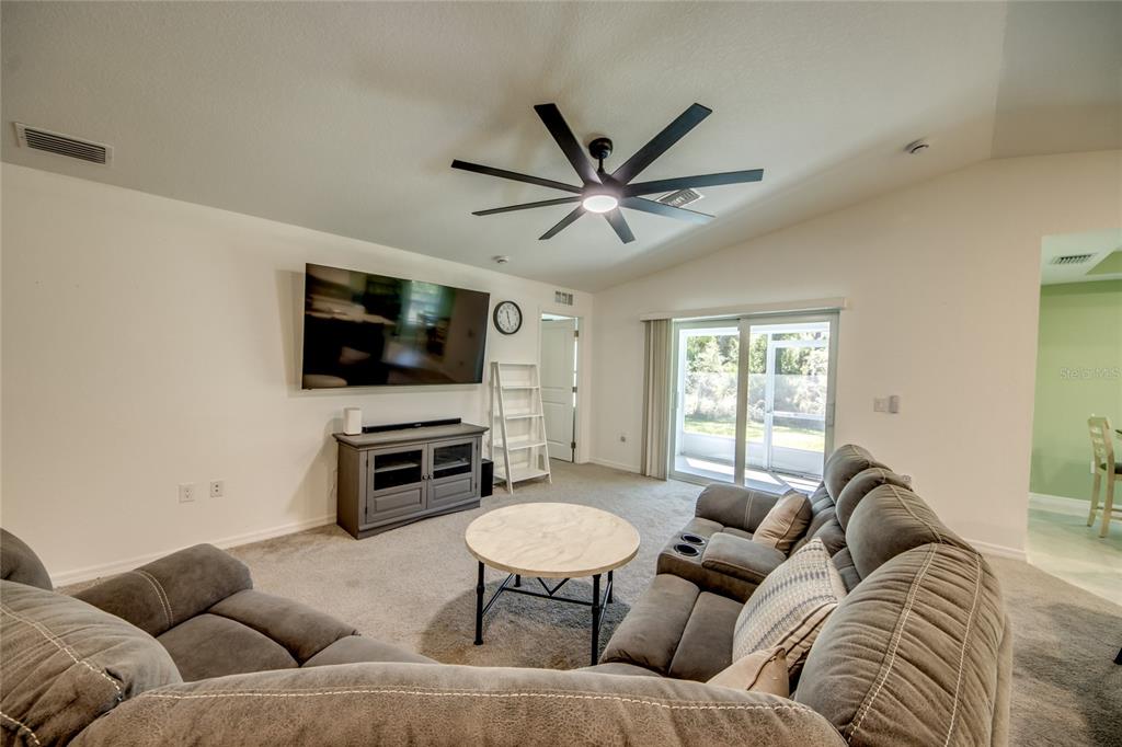 A living room features gray carpet, a large sectional sofa, a television, and a ceiling fan — 16069 EDINA AVENUE, PORT CHARLOTTE, FL