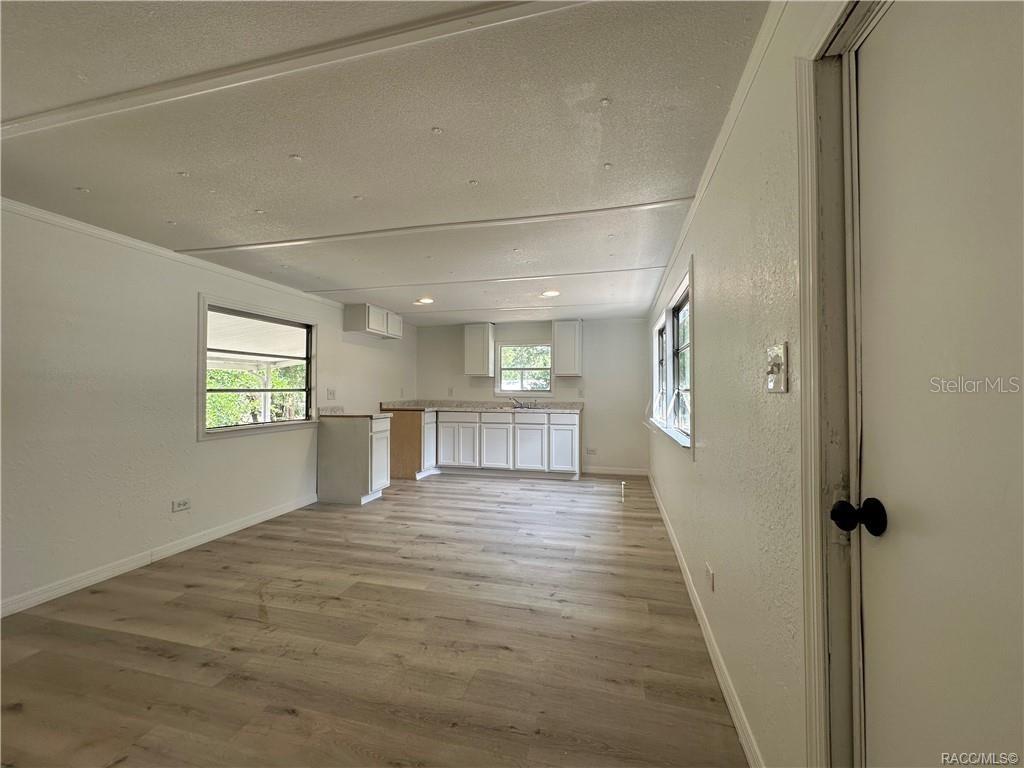 An open-concept kitchen and living area features white cabinets, light wood-look flooring, and windows — 4546 N TUMBLEWEED TRAIL, HERNANDO, FL