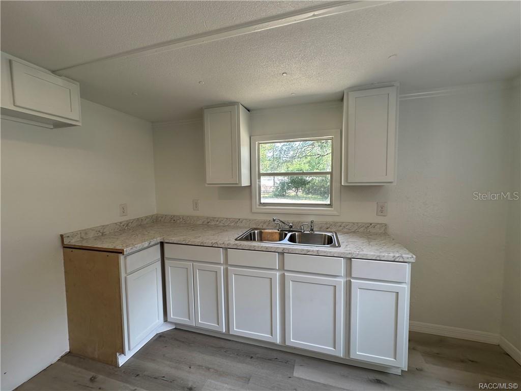 A kitchen features white cabinets, marble-patterned countertops, a double-basin sink, and light wood flooring — 4546 N TUMBLEWEED TRAIL, HERNANDO, FL
