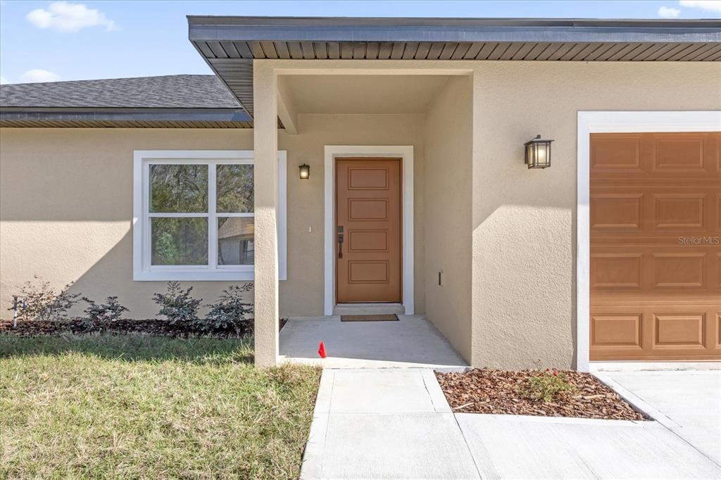 The exterior of a house features a tan stucco facade, a brown door, and a garage — 12345 SE 99TH AVENUE, BELLEVIEW, FL