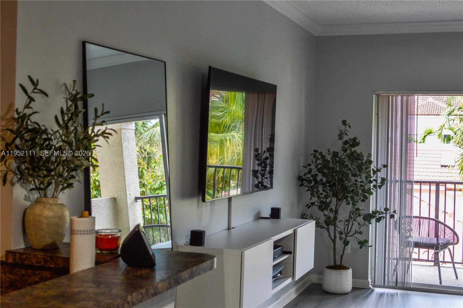 A living room features a wall-mounted television, a white media console, and a balcony view — 5840 W Sample Rd # 305, Coral Springs FL 33067, CORAL SPRINGS, FL