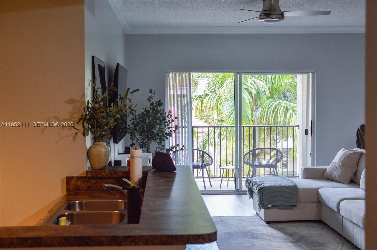 A kitchen counter overlooks a living room with a sofa and a balcony with palm trees — 5840 W Sample Rd # 305, Coral Springs FL 33067, CORAL SPRINGS, FL
