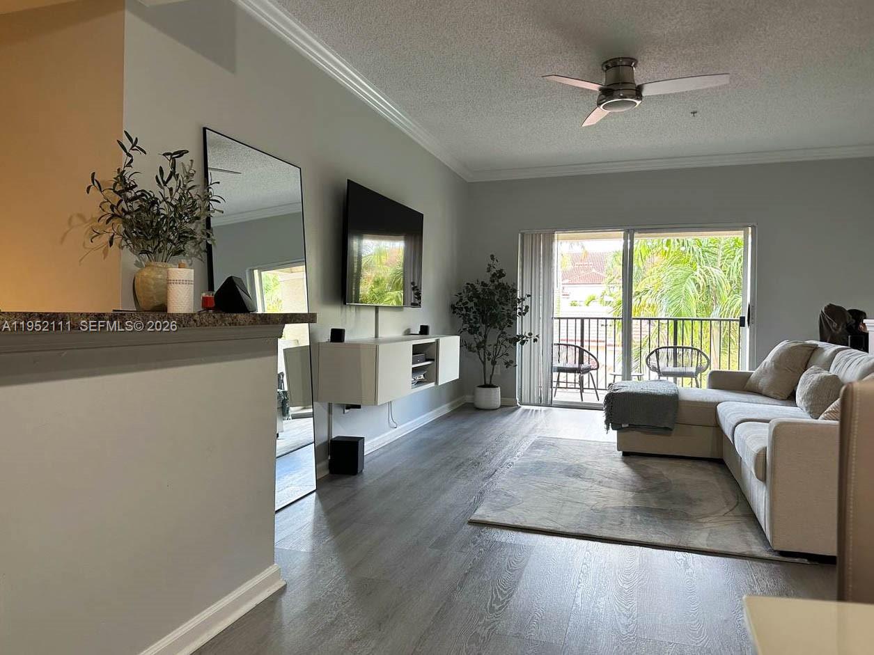 A living room features a sectional sofa, wall-mounted television, floating console, and a balcony view — 5840 W Sample Rd # 305, Coral Springs FL 33067, CORAL SPRINGS, FL