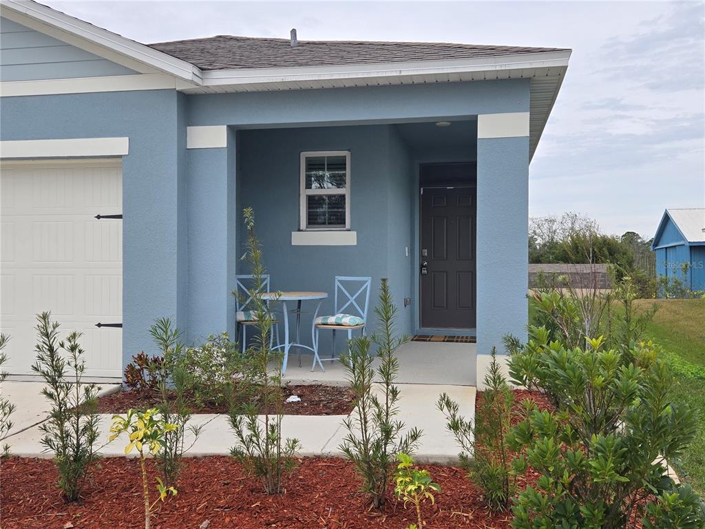 A blue house exterior features a covered front porch with a small table and chairs — 1657 ROSYDALE CIRCLE, DAVENPORT, FL