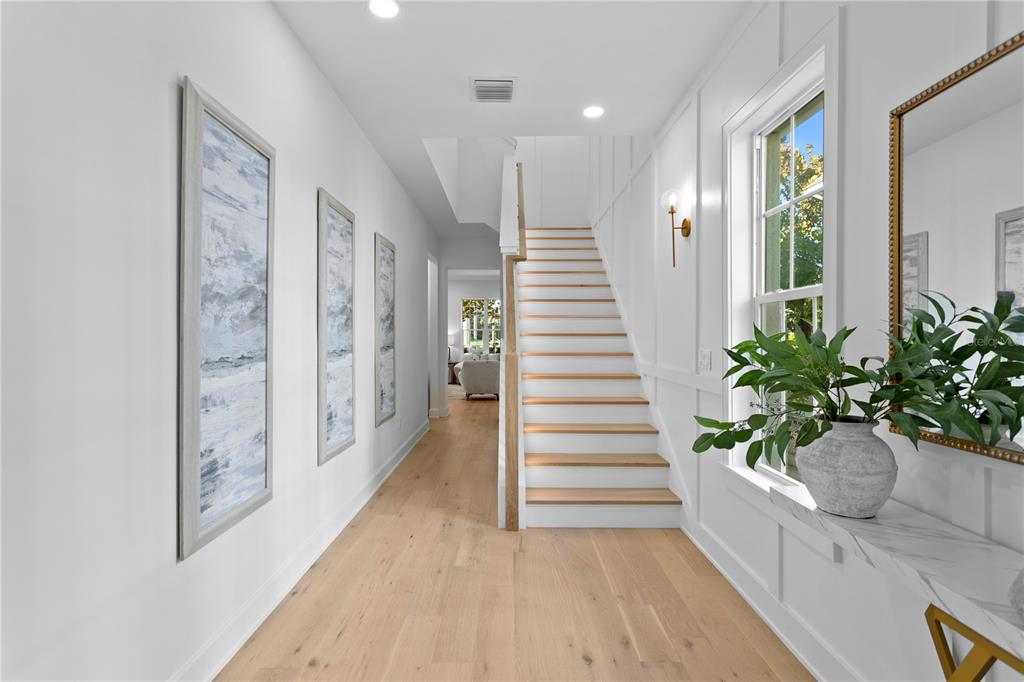 A bright entryway features light wood floors, a staircase with white risers, and wall paneling — 460 GILMAN PLACE N, ST PETERSBURG, FL