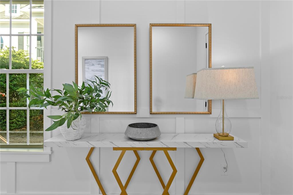 A white console table with gold geometric legs sits beneath two gold-framed rectangular mirrors — 460 GILMAN PLACE N, ST PETERSBURG, FL