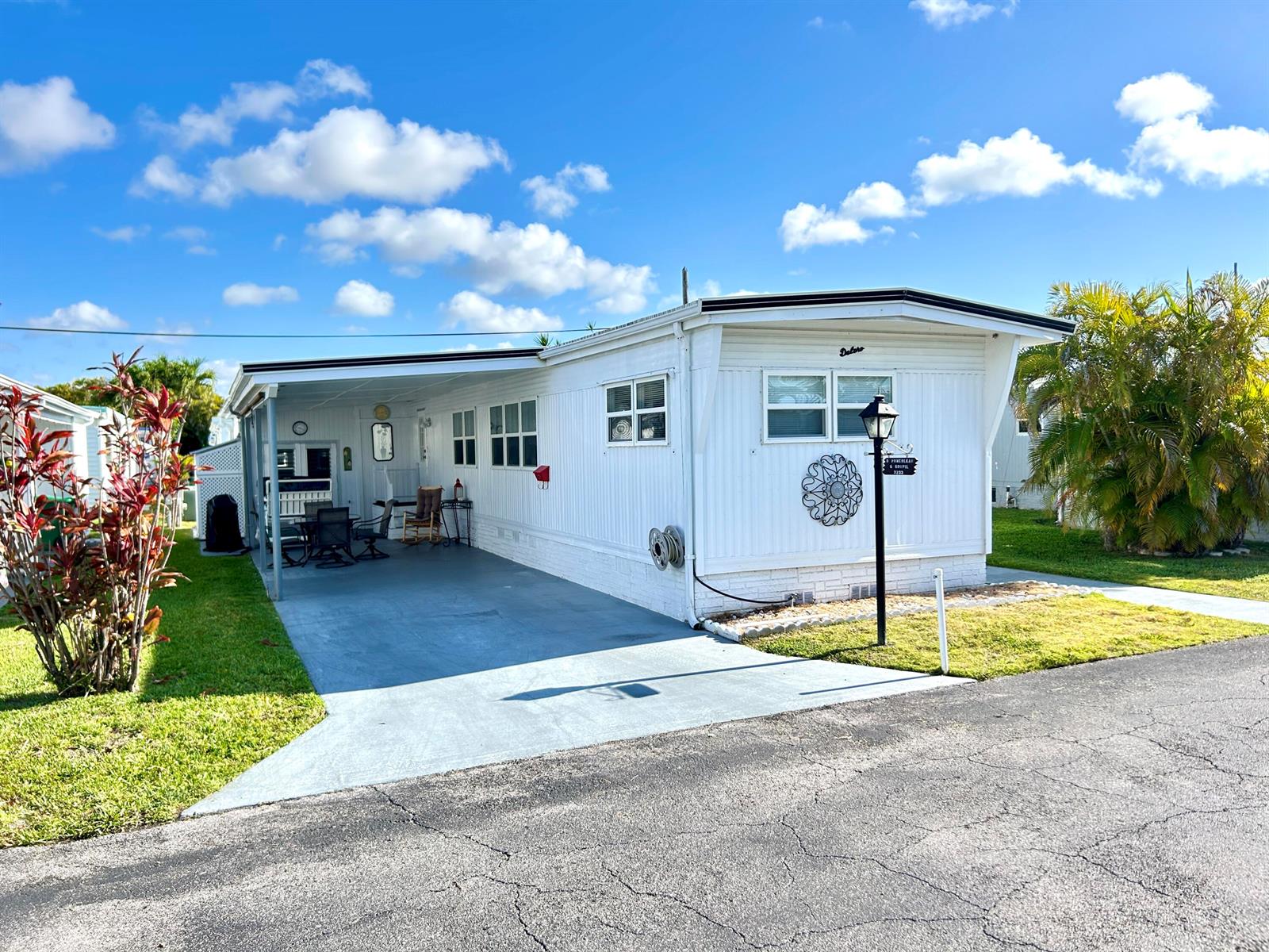 A white mobile home with a carport, driveway, and palm tree under a blue sky — 3233 State Street, Hollywood FL 33021, HOLLYWOOD, FL