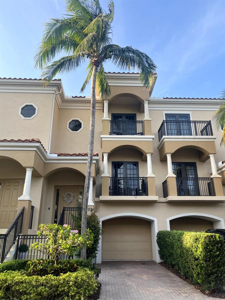 A three-story tan stucco townhouse features balconies, arched entryways, a garage, and a palm tree — 502 Del Sol Circle, Tequesta FL 33469, TEQUESTA, FL