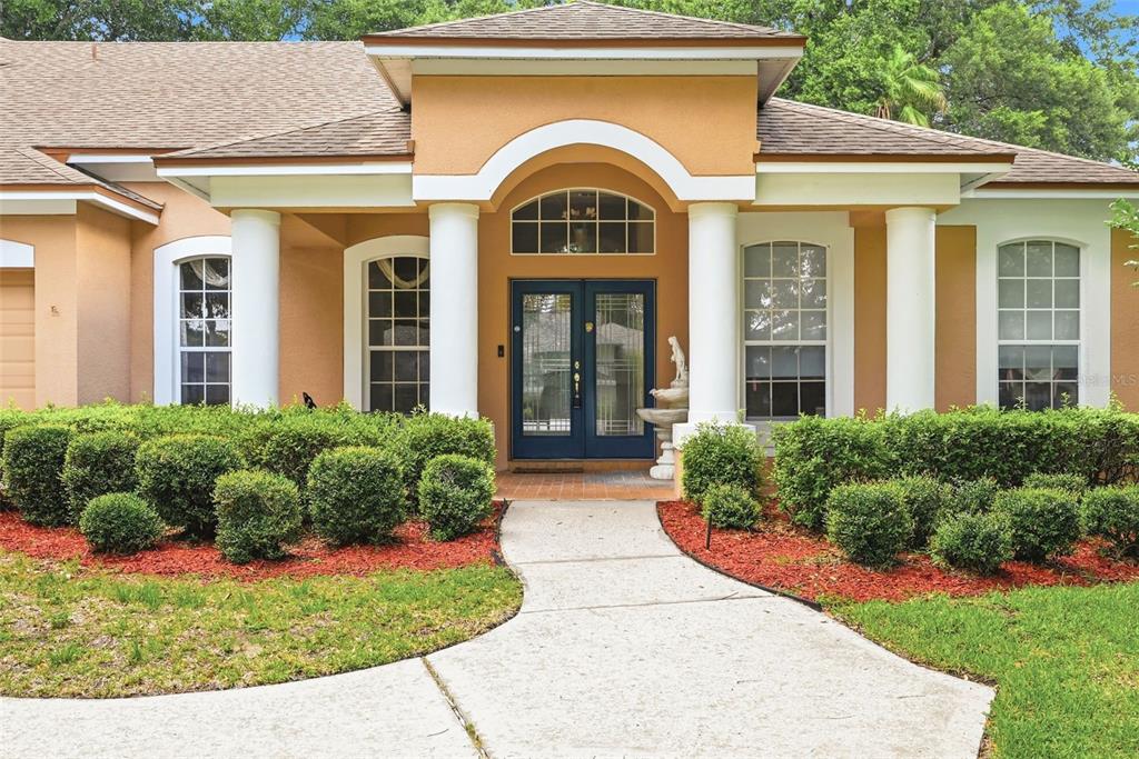 The exterior of a house features a tan facade, white columns, and a paved walkway — 483 WEKIVA PRESERVE DRIVE, APOPKA, FL