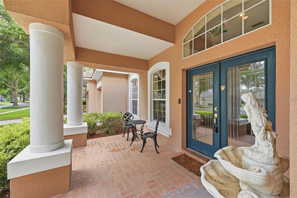 A covered brick porch features two white columns, a bistro set, and a decorative fountain — 483 WEKIVA PRESERVE DRIVE, APOPKA, FL