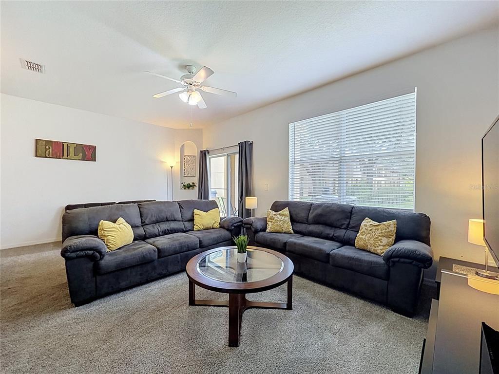 A living room features two dark gray sofas, a glass coffee table, and carpeted flooring — 220 TERRA LAGO STREET, DAVENPORT, FL