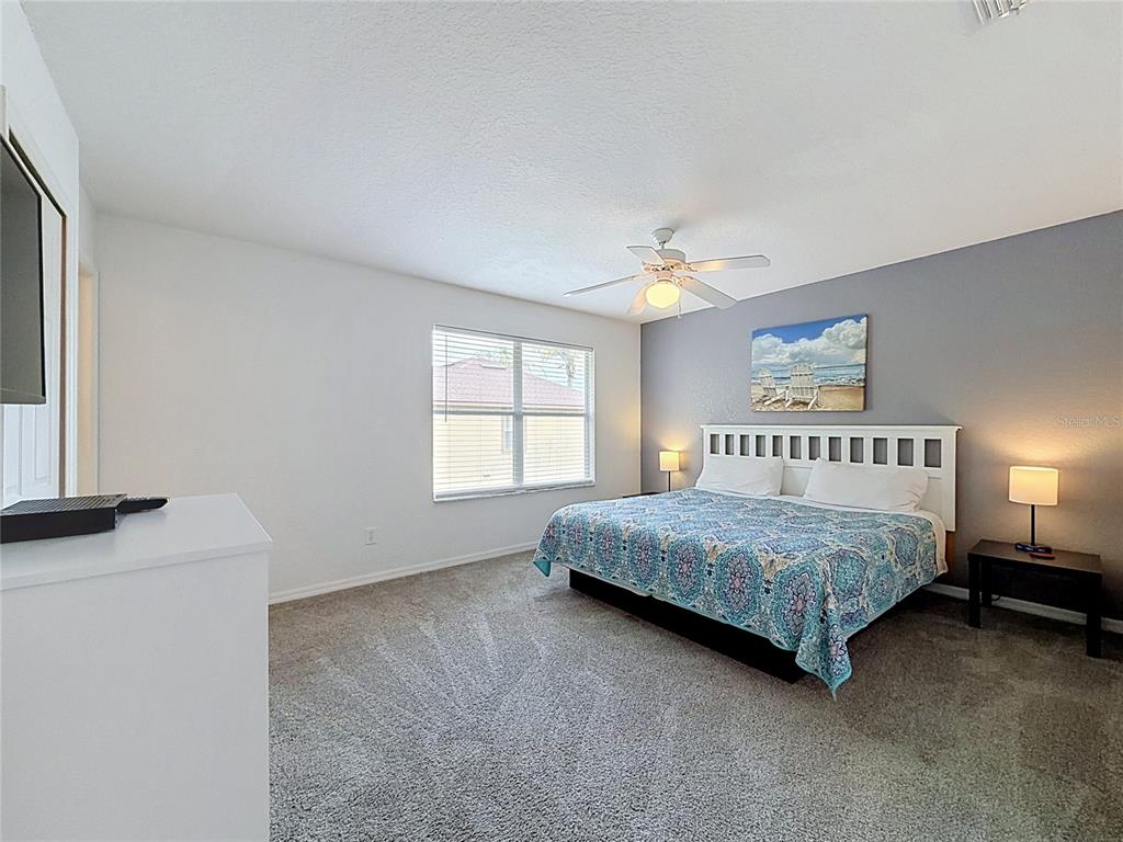 A bedroom features a king-sized bed, gray carpet, a ceiling fan, and a gray accent wall — 220 TERRA LAGO STREET, DAVENPORT, FL