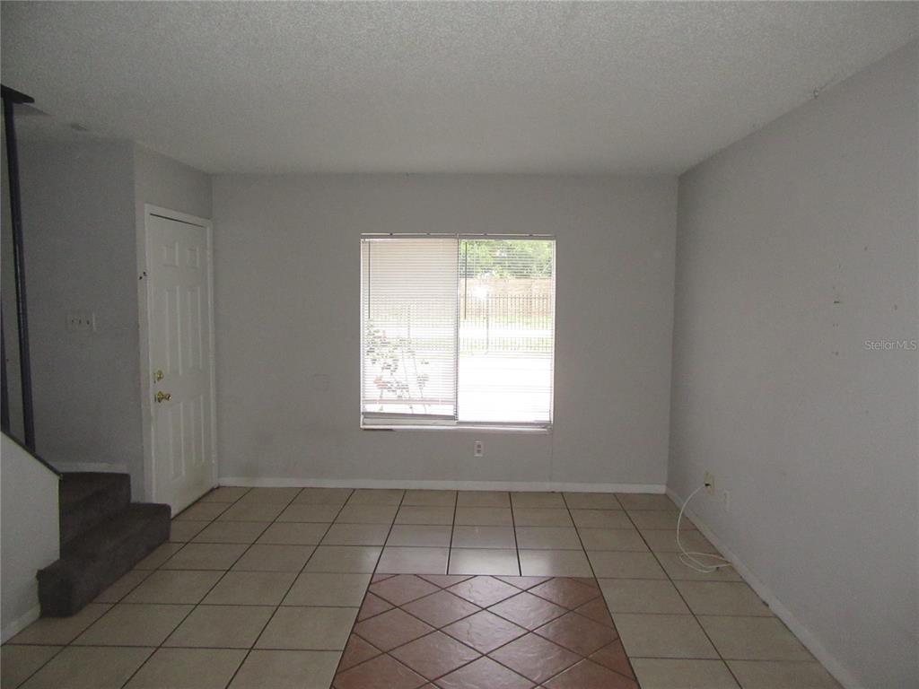 An empty room features light-colored tile flooring, a central accent tile section, and a window — 13050 N 20TH STREET, TAMPA, FL