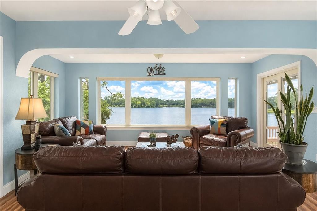 A living room with brown leather furniture overlooks a lake through large windows — 1081 NE 130TH TERRACE, SILVER SPRINGS, FL