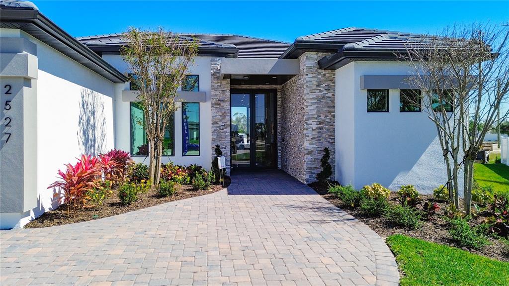 A modern house exterior features a stone-accented entryway, paver walkway, and white stucco walls — 2527 GLEASON PARKWAY, CAPE CORAL, FL