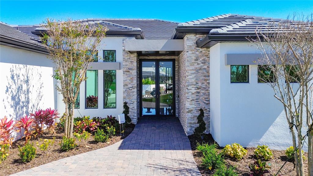 The exterior of a modern house features a stone-accented entryway and a paved walkway — 2527 GLEASON PARKWAY, CAPE CORAL, FL