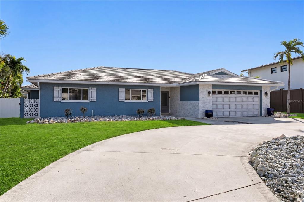 A blue single-story house with a white stone garage facade and a concrete driveway — 10038 S YACHT CLUB DRIVE, TREASURE ISLAND, FL