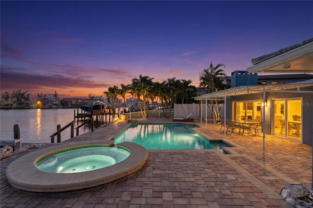 A backyard patio features a pool, a circular hot tub, and a view of water — 10038 S YACHT CLUB DRIVE, TREASURE ISLAND, FL