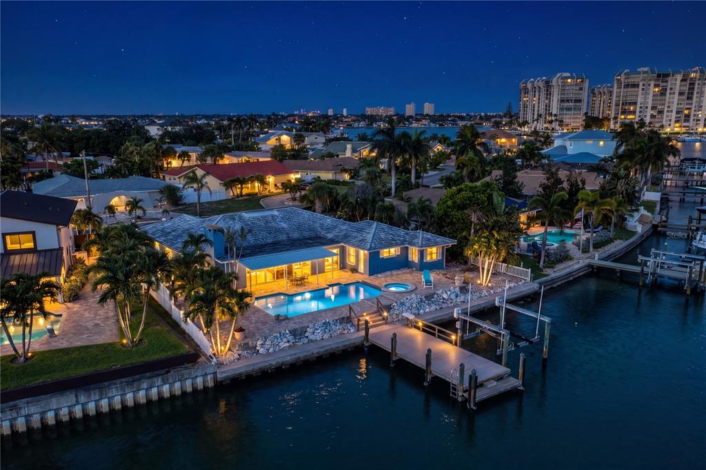An aerial night view of a waterfront house featuring a pool, dock, and palm trees — 10038 S YACHT CLUB DRIVE, TREASURE ISLAND, FL